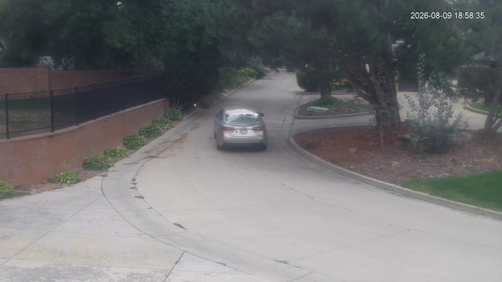 A silver sedan driving away on a curved residential street