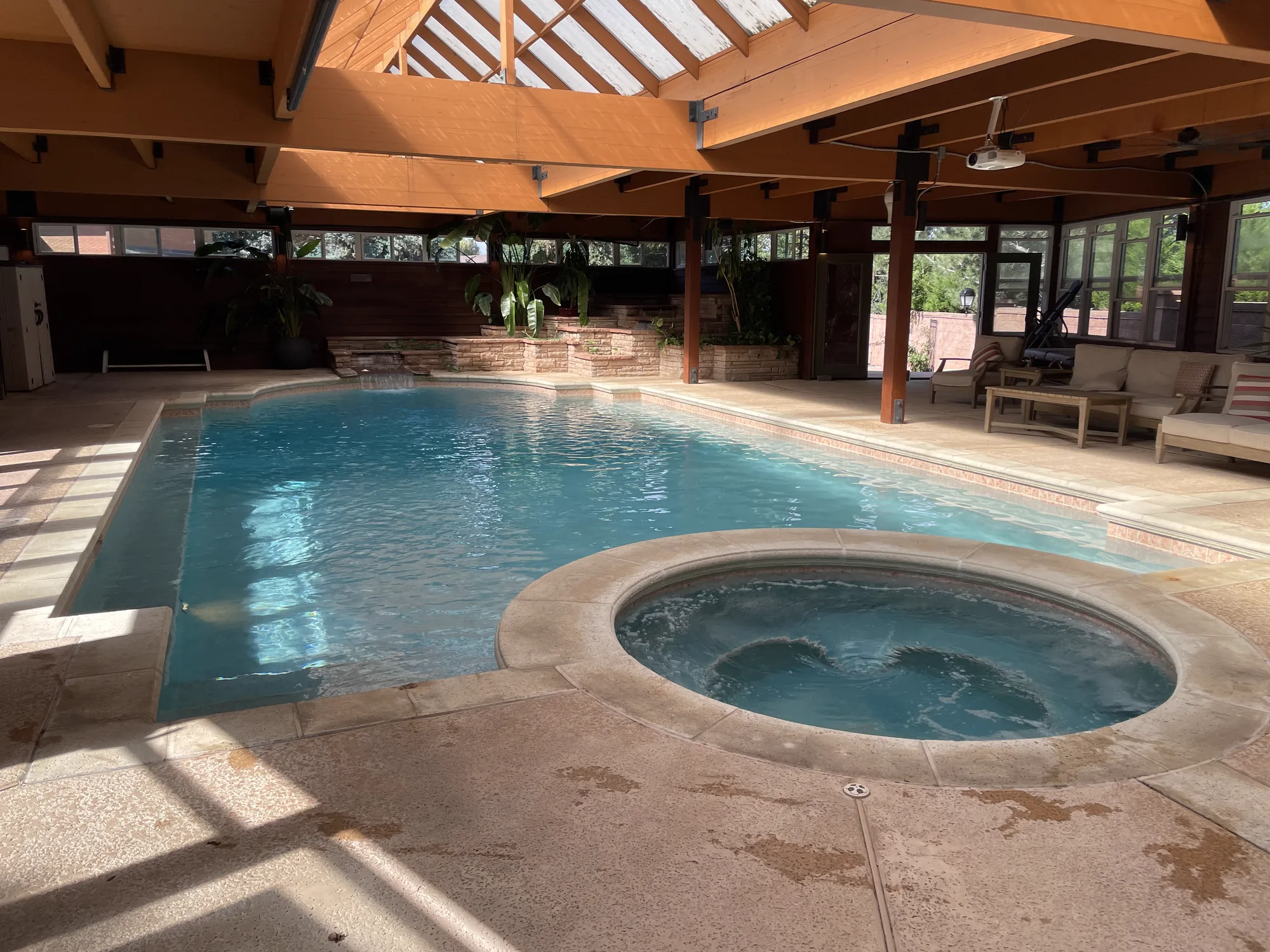 An indoor swimming pool and attached spa beneath a timber-framed roof with skylights